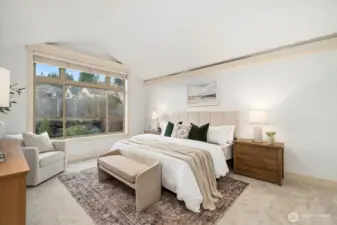 Serene primary suite with soaring vaulted ceiling & expansive window framing backyard garden views.