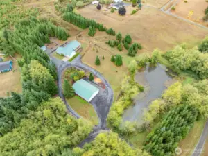 Aerial view capturing the full beauty of the home, shop, pond, and acreage.