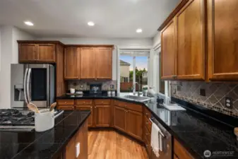 Large kitchen with cared-for cabinetry, granite countertops, stainless appliances, gas range with downdraft, tiled backsplash and dreamy corner kitchen sink area. The island comfortably seats 4-5 in addition to the eat-in dining area adjoining the kitchen. The kitchen is well-lit. Gleaming hardwood flooring.