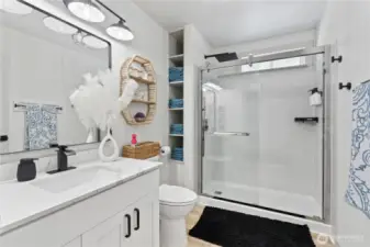 This beautifully remodeled bathroom offers a spa-like experience with a sleek walk-in shower, quartz countertop, matte black fixtures, and built-in shelving for added storage. Woven textures, soft lighting, and modern finishes blend to create a stylish yet functional space that feels fresh and luxurious.