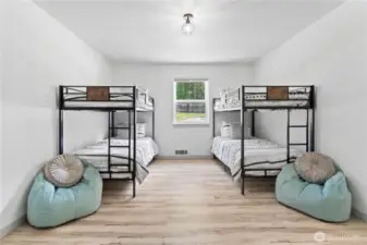 Designed with versatility and family in mind, this large bunk room features two twin-over-twin beds, plush seating areas, and durable wood-look flooring. Crisp white walls and a central window bring in abundant light, making it ideal for kids, guests, or vacation rental use.