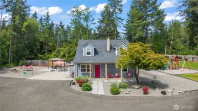 This crisp daytime shot showcases the home's inviting front exterior with fresh landscaping, a covered porch, and a bold red door that makes a memorable first impression. The expansive, well-designed backyard includes a patio with gazebo, fire pit seating area, and dedicated playground space—all beautifully laid out and easy to maintain. Ideal for families, entertainers, or those seeking tranquility with modern comforts.