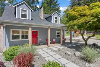 This inviting front entry blends rustic charm with modern updates. A vibrant red door, warm wood columns, and fresh landscaping welcome you home. The stone path adds elegance and functionality, while the nearby tree and view of the playground space highlight the home’s family-friendly design and thoughtful outdoor planning.