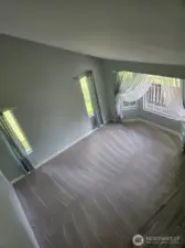 Aerial view of the sun-filled living room highlights soaring vaulted ceilings, tall windows, and fresh carpet. This elegant entry space sets the tone for warmth and brightness throughout the home.