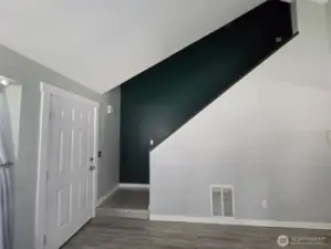 Modern entryway with striking vaulted ceilings and a bold accent wall along the stairwell. Tile flooring flows into the main living area, adding a clean, contemporary touch to the home's layout.