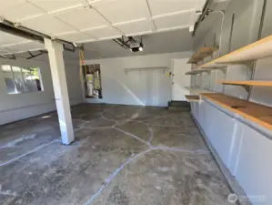 Spacious two-car garage with automatic openers and overhead lighting offers plenty of room for vehicles, tools, and hobbies. A built-in workbench and wall shelving provide ideal organization for any DIY enthusiast.