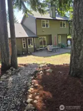 A natural woodland path leads from towering evergreens to the home's back patio, offering a seamless transition between nature and outdoor living. This backyard retreat blends tranquility with usability.