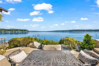 Step from the great room to a stunning waterside patio framed by lush landscaping, a carved granite bench, and serene southern views.