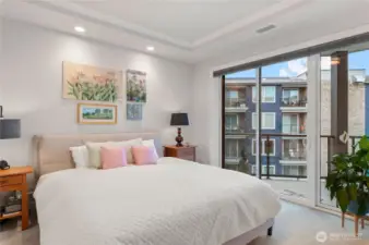 Spacious primary suite highlighted by tray ceilings, soft natural light, and sliding doors to the balcony