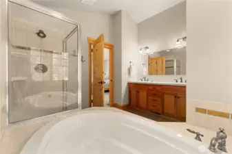 Luxurious primary bathroom featuring a soaking tub, walk-in tile shower, and dual vanity with warm wood cabinetry.