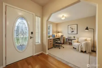 A welcoming entry begins with rich hardwood flooring and a striking front door featuring an elegant glass insert that fills the space with natural light. Just beyond, an open flex room framed by architectural detailing offers endless possibilities — ideal for a home office, formal sitting area, or additional living space.