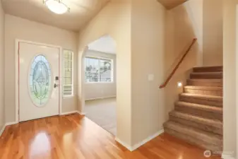 Welcome home to warmth, light, and timeless detail. Gleaming hardwood floors and a decorative glass entry door create a bright and inviting first impression, while an elegant architectural opening reveals a versatile flex room just beyond. The staircase, accented with a warm wood railing and integrated step lighting, adds both safety and sophistication — a graceful transition that sets the tone for comfort and refined living throughout.