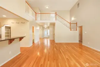 The open-concept great room showcases soaring ceilings and an elegant upper-level overlook that enhances the home’s sense of space and architectural presence. Rich hardwood flooring flows throughout, connecting the living area seamlessly to the kitchen and inviting breakfast bar. The graceful staircase with wood-accented railing adds dimension and character, while the expansive layout creates an airy, light-filled environment designed for both everyday comfort and effortless entertaining.
