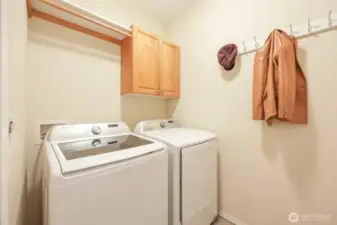 The dedicated laundry room with oversized washer and dryer offers convenience and efficiency, featuring upper cabinetry for additional storage and a hanging rod for air-drying or organization. Designed with practicality in mind, the space keeps daily tasks neatly tucked away while maintaining easy accessibility.