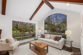 The living room impresses with soaring vaulted ceilings, exposed wood beams, and expansive picture windows that fill the space with natural light.