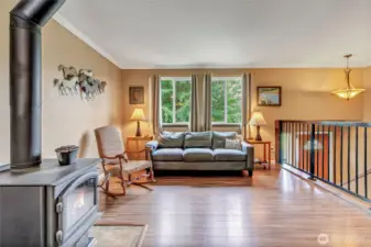 Cozy and light-filled living area featuring a wood-burning stove, scenic outdoor views, and warm laminate flooring—perfect for relaxing or gathering with guests.