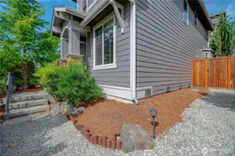 Front corner of home with dual steps off front porch for easy access around the side of the house with fresh gravel and beauty bark.
