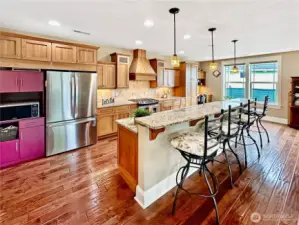 Beautiful kitchen with slab granite counters with tile back splash, island with eating bar, prep desk, stainless appliances and oak cabinets.