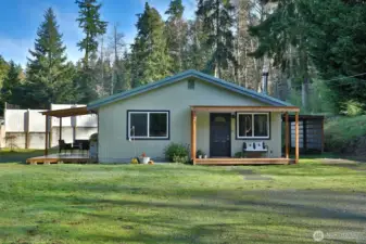 Sweet covered front porch entry in addition to a covered deck and covered storage area (or carport for a small vehicle). Windows to the left are in the kitchen and to the right, the living room.