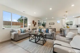 Bright open-concept living room with large windows, recessed lighting, and seamless flow to the dining and kitchen areas.