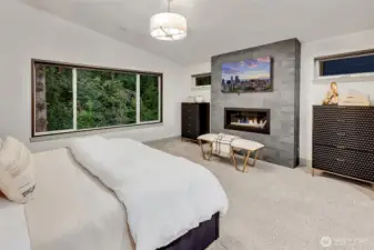 Overlooking a private forest, the serene bedroom features a floor-to-ceiling gas fireplace and remote-control black out shades.