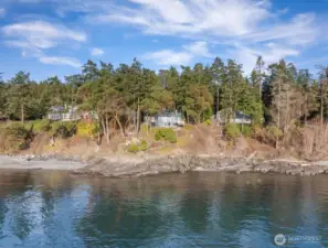 Striking west-facing residence positioned above the shoreline, surrounded by Madrona trees and layered marine vistas.