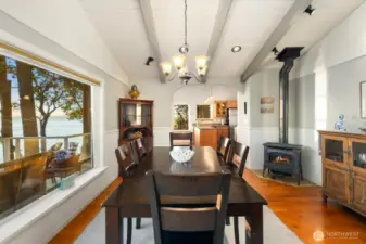 Dining space featuring wood stove, vaulted ceilings, and large picture windows capturing tranquil waterfront scenery and natural light.