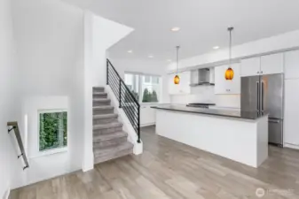 The entry stairs to the left. The stairs to the second level in the middle and the island kitchen to the right.