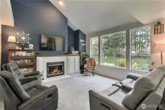 Spacious Family Room featuring a cozy fireplace, soaring cathedral ceilings that enhance the sense of openness, a large picture window that floods the space with natural light, and a beautifully appointed interior with tasteful, elegant color choices.