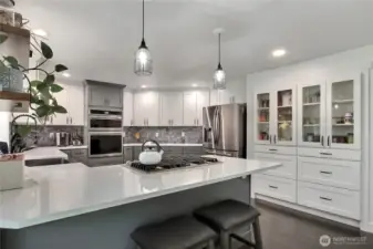This kitchen boasts ample counter space, complemented by stylish glass cabinets that showcase beautiful dishware, and the convenience of a built-in wall oven for efficient cooking.