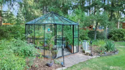 A captivating glass greenhouse, elegantly nestled amidst lush greenery, features a welcoming brick entry that adds a touch of rustic charm and architectural interest to the scene.