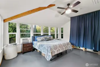 Large sunroom currently being used as primary bedroom, with ceiling fan and exposed beams