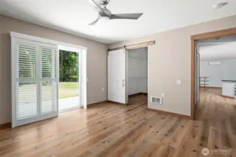 Primary bedroom with large walk in closet with a custom sliding barn door and glass slider with shutters to the back patio.