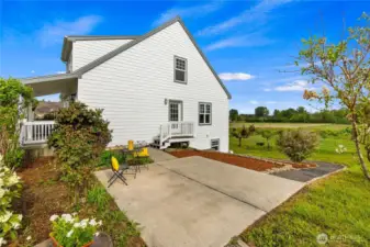 Side view of the home with a Trex deck & patio between the house and the barn. A gravel pathway leads to the lower level of the home & terraced garden beds along the path provide great gardening opportunities!