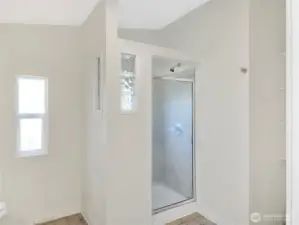 Spacious primary bath featuring a large tiled walk-in shower, linen storage, and natural light from glass block accents and a decorative window.