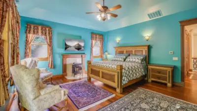 The room features a cozy fireplace, elegant wood detailing, and ample space for seating, offering both comfort and style. With high ceilings and abundant natural light, this bedroom is a tranquil oasis designed for relaxation.