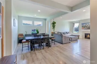 Open, bright, and beautifully connected—this main living space seamlessly blends the dining and family rooms with large windows, warm flooring, and a cozy fireplace as the focal point.