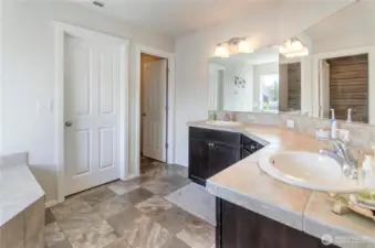 This elegant en-suite bath features dual vanities, tile countertops and flooring, and a spacious layout designed for both comfort and convenience.