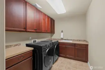 This large laundry room is thoughtfully designed with ample cabinets, expansive countertops, and a built-in sink for everyday convenience.