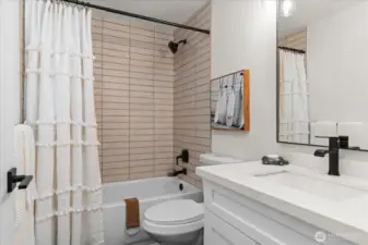 Tastefully appointed main full bath with white cabinets, quartz countertop, and subway tile tub surround
