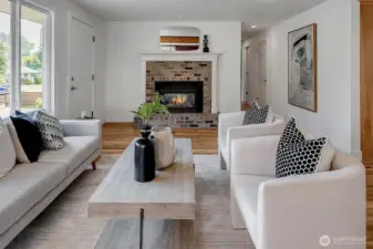 Bright and open living room featuring large picture windows, hardwood floors, and a fireplace centerpiece