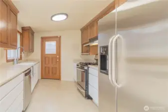 Good size kitchen with two-toned cabinets, stainless appliances, custom Corian counters with bonus cutting board but-outs, with slider to deck
