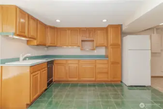 Basement kitchen area has tile flooring, sink, dishwasher and fridge, no heating element