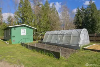 Two hoop-style greenhouses, raised garden beds, and detached outbuilding ideal for shop, studio, or flexible use.