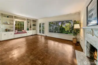 Bathed in natural light and graced with original hardwood parquet floors, this spacious main living area invites both quiet reflection and joyful gathering. A picture window anchors the room with a verdant forest view, while custom built-ins, a cozy window seat, and an elegant fireplace framed in marble lend warmth and character. The thoughtful craftsmanship reflects the home’s timeless charm, creating a place of comfort that feels rooted in its surroundings.