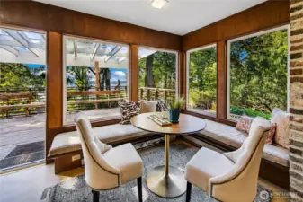 Wrapped in windows and warmth, this cozy corner nook offers a perfect perch to begin your day or unwind at dusk. Surrounded by lush woodland and filtered lake views, the built-in seating and natural wood paneling evoke a sense of timeless comfort. Just beyond, the adjacent patio and trellis-covered outdoor space blur the line between inside and out—offering a serene setting for slow mornings, afternoon tea, or gathering with friends amid the tranquility of the Evergreen Lakeshore Preserve.