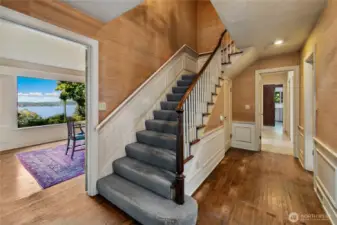 This gracious entry hall sets the tone for the home’s timeless character, with classic millwork, original hardwoods, and a sweeping staircase that hints at the history held within these walls. Natural light spills in from surrounding rooms, offering glimpses of lake views and garden greenery beyond. The layout invites both formal entertaining and everyday ease, connecting the heart of the home with its peaceful lakeside setting.