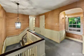 At the top of the stairs, this second-floor landing offers a moment of pause and quietude, surrounded by warm wood paneling and traditional wainscoting. A large window frames views of the forested grounds, drawing the natural beauty of the setting indoors. This spacious corridor connects the upper-level bedrooms and provides a lovely perch from which to admire the home's classic architectural details.