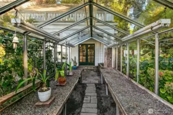 A hidden gem tucked within the landscape, this vintage glass greenhouse invites year-round cultivation and quiet retreat. Framed by lush plantings and outfitted with classic potting benches, the structure echoes a time when estate gardens were both productive and poetic. A pair of green French doors anchors the far end, offering an elegant connection between garden and home.
