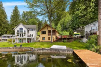 Front of home featuring spacious side deck, dock, and yard perfect for entertainment.